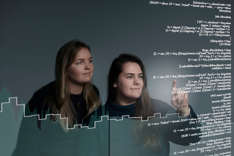 Two young female employees looking at algorithms on a screen.