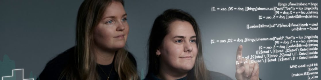 Two young female employees looking at algorithms on a screen.