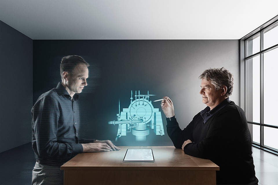 Wouter diskuterer en kompressor i et virtuelt møte med en kollega. Den digitale tvillingen er illustrert gjennom grafikk på toppen av det faktiske bildet.