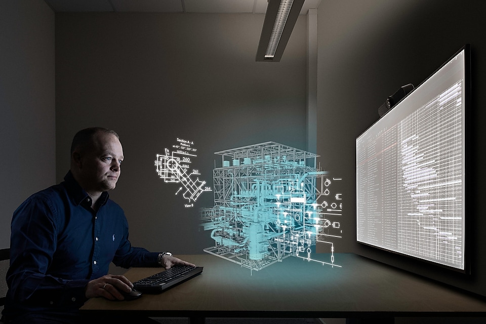 tommy jobber i et møterom foran en stor skjerm, med den digitale tvillingen illustrert gjennom grafikk på toppen av det faktiske bildet. 