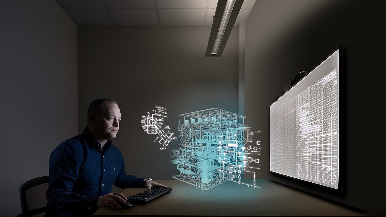 tommy jobber i et møterom foran en stor skjerm, med den digitale tvillingen illustrert gjennom grafikk på toppen av det faktiske bildet.