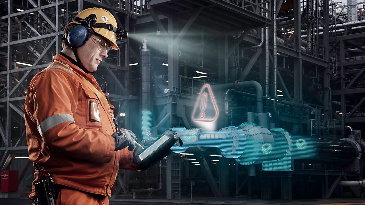 alexander jobber med en iPad ute på anlegget. Vi ser store rør i bakgrunnen, og den digitale tvillingen illustrert gjennom grafikk på toppen av det faktiske bildet.