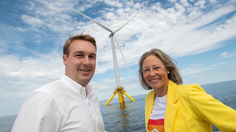 To Shell-ansatte poserer foran TetraSpar Demonstrator: en flytende havmølle i drift utenfor kysten av Haugesund.
