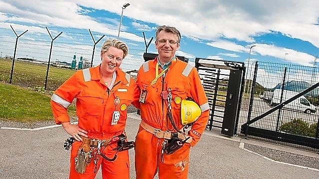 Bilde fra nyere tid: To ansatte i kjeledress står foran porten ved Nyhamna prosessanlegg i Aukra kommune.