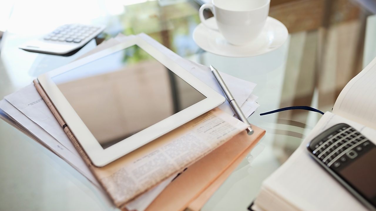 Tablet computer, newspaper, coffee cup and cell phone on desk