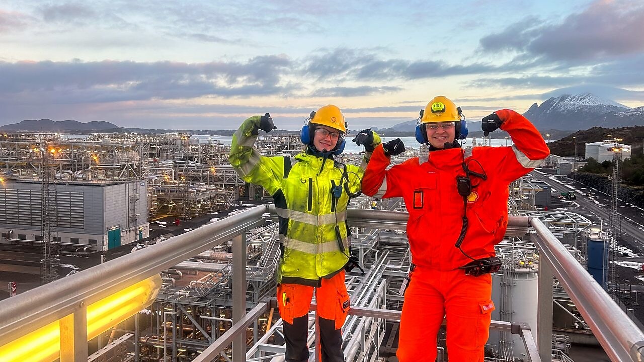 Mia og Elvin står på en modul ute på Nyhamna prosessanlegg. De smiler og viser muskler.