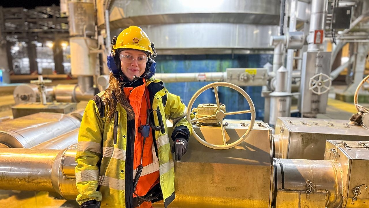 Mia står ved prosessutstyret på Nyhamna, iført Shell-kjeledress og personlig verneutstyr.