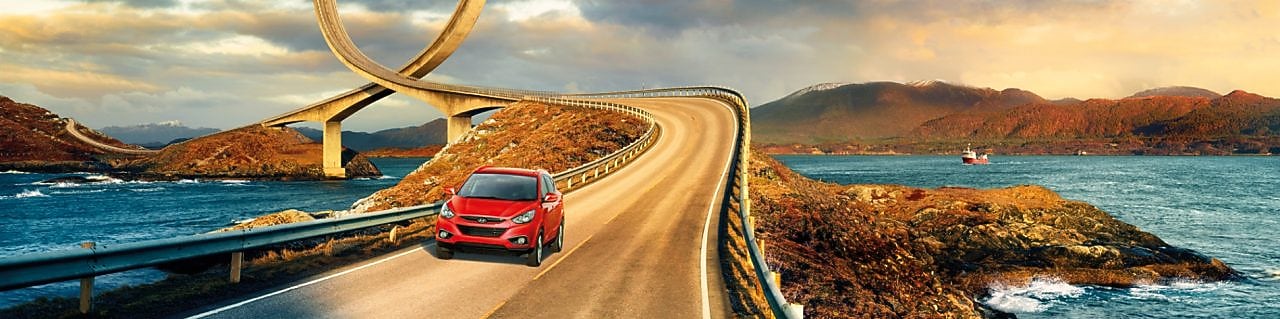 Rød bil kjører på vei ved elv