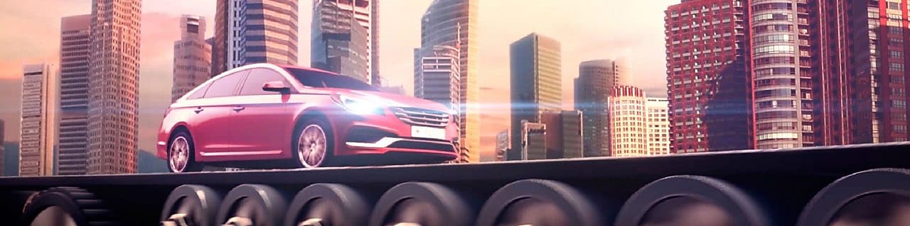 Rød bil kjører med frontlyktene på med silhuett av by i bakgrunnen